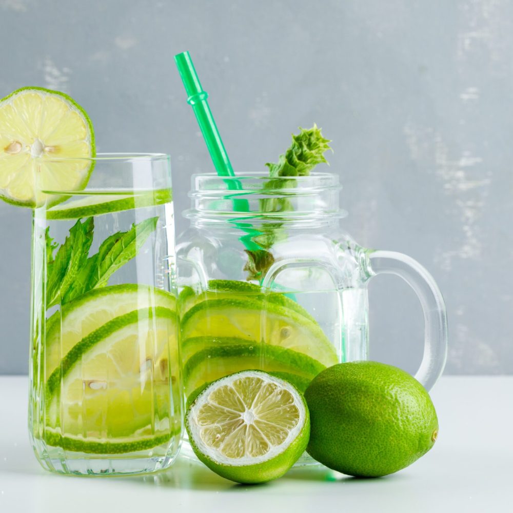 Lemonade in glass and mason jar with lemon, herbs, straw side view on white and plaster background